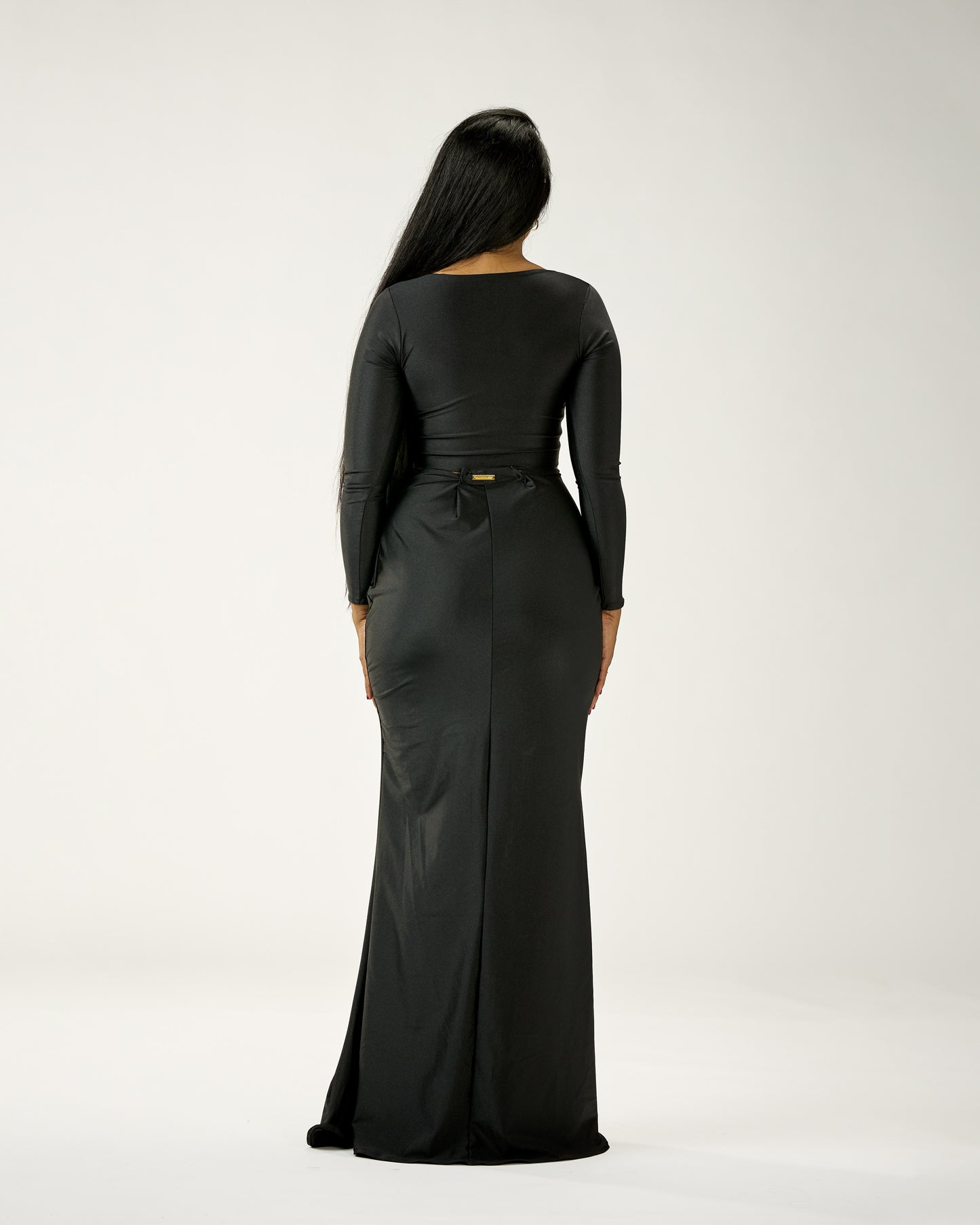 Person wearing a black long-sleeve dress with a belt on a white background